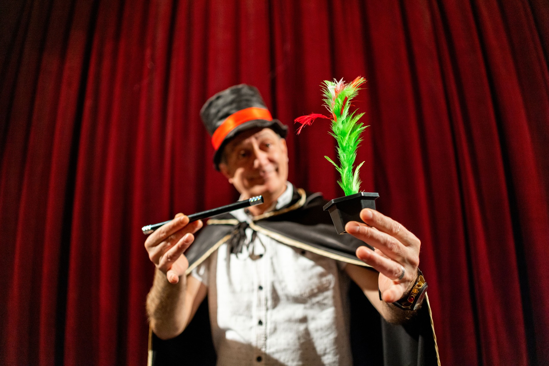 Senior male magician performing magic tricks with wand and fake flowers on the stage at the theatre